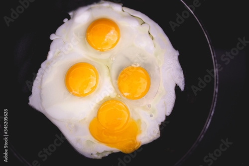 Fried eggs in frying pan. Four eggs. Making breakfast for family. Family weekend breakfast. Quick easy brunch breakfast. Over medium fried eggs. Egg yolk, egg whites. Black stove top. Broken egg yolk