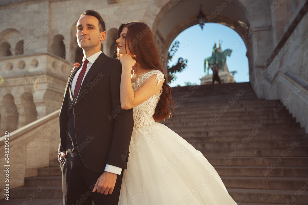 Naklejka premium Bride and groom hugging in the old town street. Wedding couple walking on the Fisherman's Bastion, Budapest, Hungary. Happy romantic young couple celebrating their marriage. Wedding and love concept.