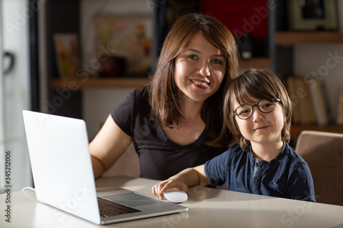 Mother and boy studying with laptop in home.