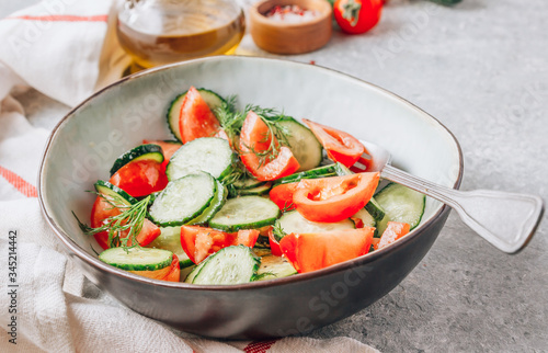 Healthy vegetable salad of fresh tomato  cucumber  dill and spices and oil in bowl on light gray background. Diet concept.