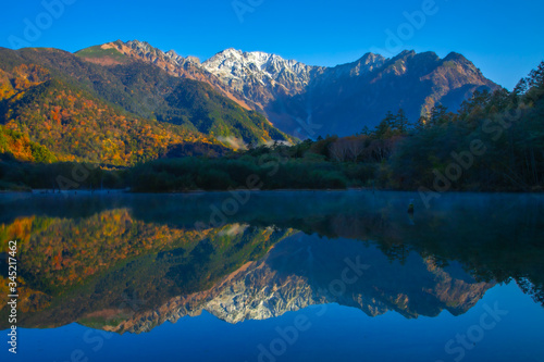 紅葉の上高地大正池から初冠雪した穂高連邦と水面に鮮やかに映り込み水鏡の風景写真