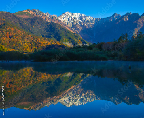 紅葉の上高地大正池から初冠雪した穂高連邦と水面に鮮やかに映り込み水鏡の風景写真