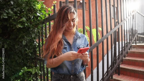 Latin woman smiling and using smartphone, Standing with sunset