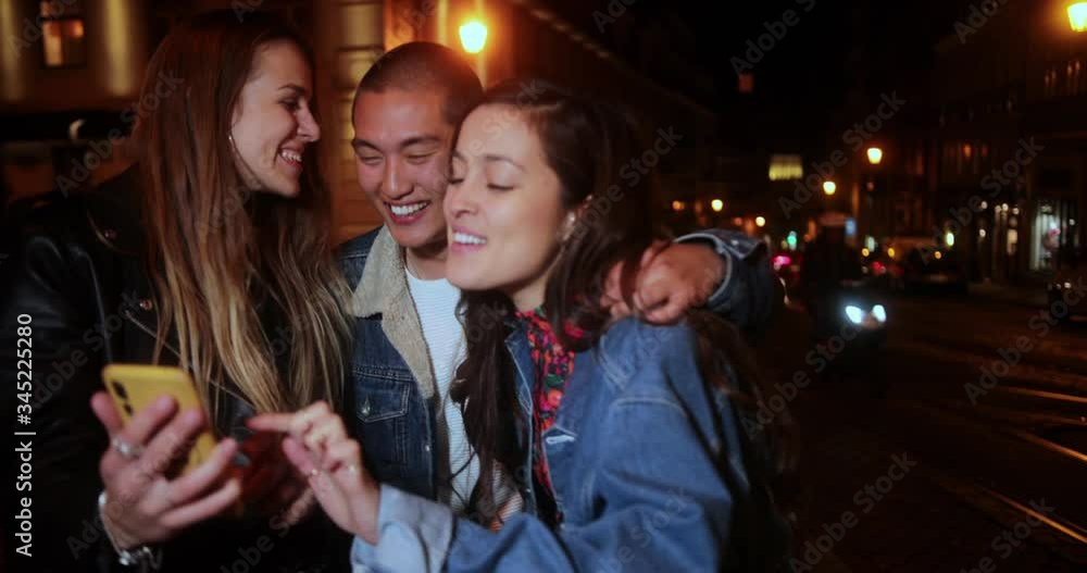 Multi-ethnic group of friends watching video on smartphone on street Multi-ethnic group of friends watching video on smartphone on street