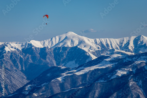 Paragliding flies in winter in the blue sky high above the Caucasus mountains