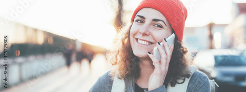 Curly handsome woman talking on the phone on the street, wearing backpack and smiling. Wide screen, panoramic