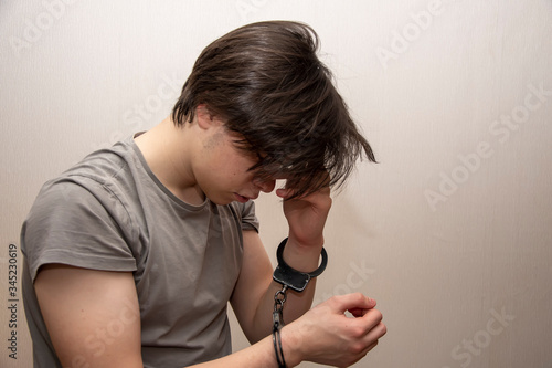Valokuvatapetti Portrait of a sad teenager in handcuffs on a gray background, medium plan
