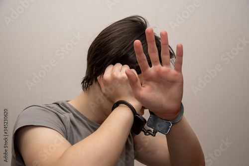 Obraz na plátně A handcuffed teenager covers his face with his hands on a gray background, medium plan