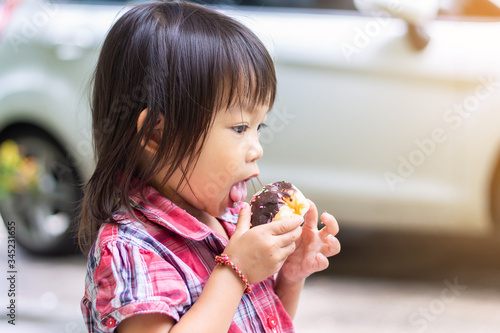 Selective    focus.    Portrait    image    of    2-3    years    old    of    baby.    Happy    Asian    child    girl    eating    some    sweet    donut or    chocolate    bread.    Kid    and    food    concept.