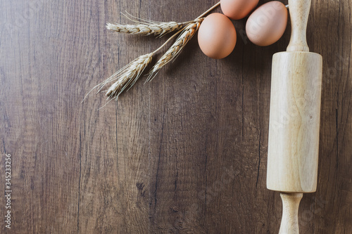 Rolling dough and Dry wheat grains with eggs on the brown wooden table, From top view. photo