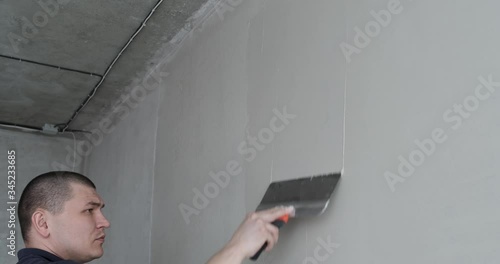 Young man aligns wall with construction equipment. Wall preparation is carried out in accordance with design project in new apartment. Putty on wall for smooth walls. Quality repairs. plastering wall photo