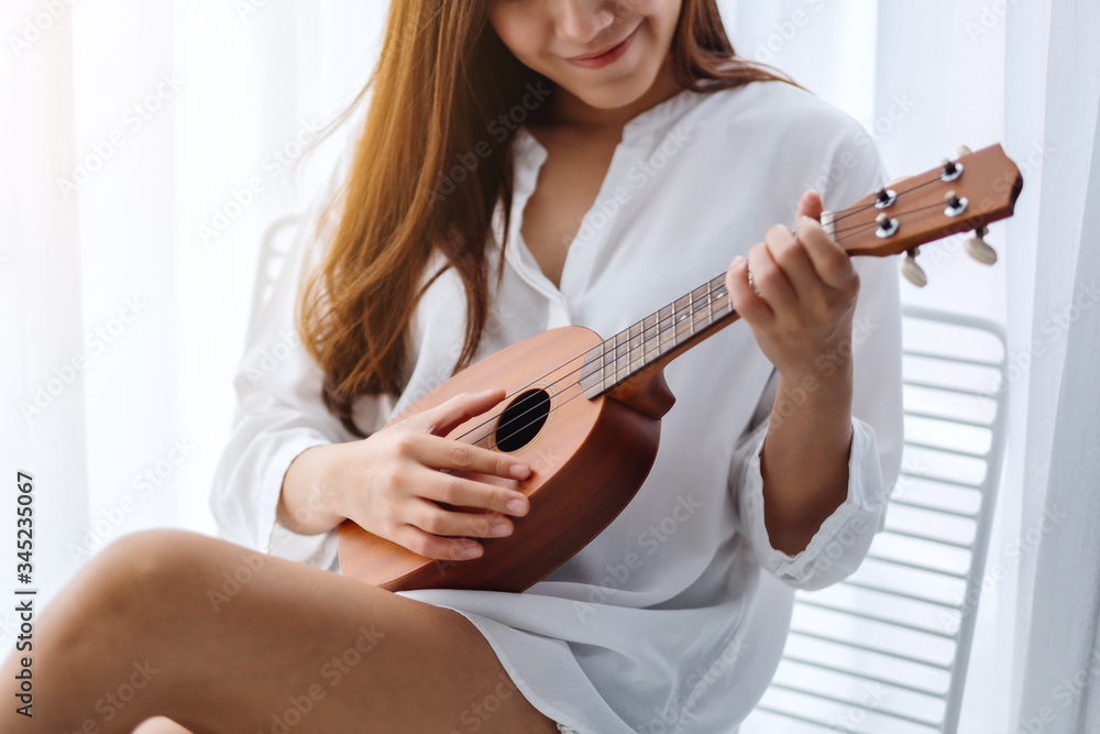A beautiful asian woman sitting and playing ukulele in bedroom A beautiful asian woman sitting and playing ukulele in bedroom