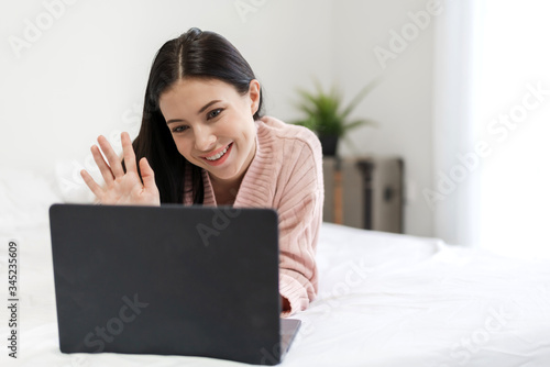 Smiling of young beautiful pretty woman relaxing and using technology laptop computer lying on bed and joyful on weekend in the bedroom.girl checking social apps and working.technology online concept