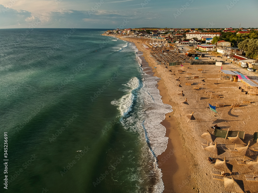 Aerial view of amazing beach with umbrellas and turquoise sea at sunrise. Black Sea at Vama Veche, Romania