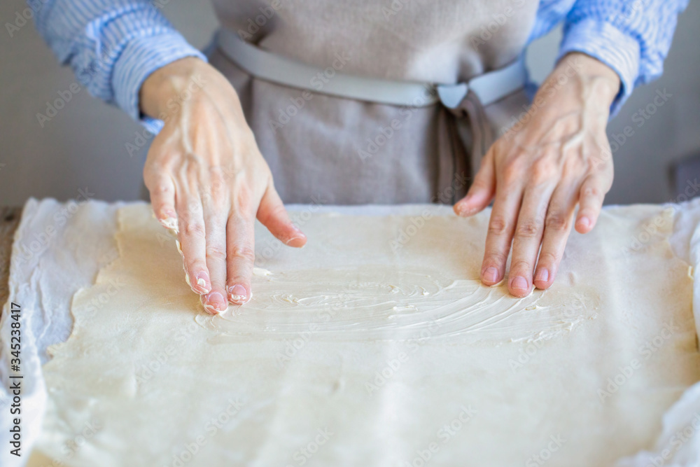 Butter the dough. Cooking apple strudel. Girl is preparing a pie at home in an apron. Work with puff pastry. Hands in oil. The process of making apple strudel
