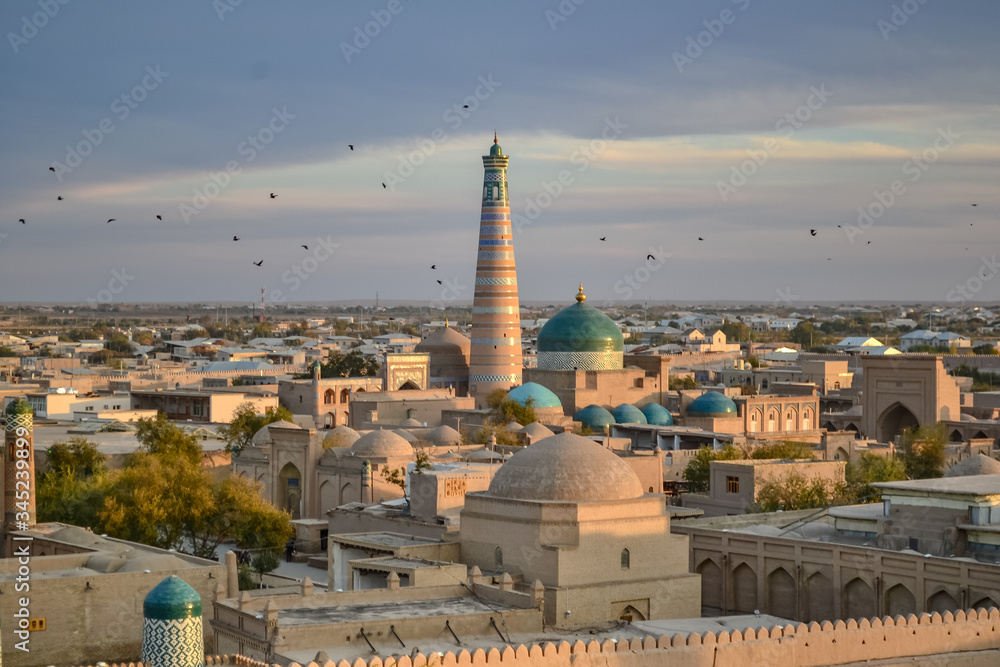 Beautiful cityscape with large islamic minaret over Khiva, Uzbekistan, seen from air during sunset, with birds in sky