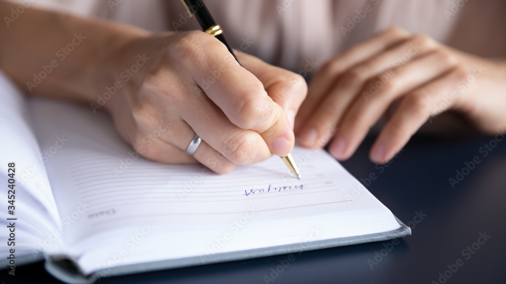 Close up female hand holding pen, writing information in notebook, young female businesswoman planning day, making notes, handwriting, student preparing for exam, studying at home Close up female hand holding pen, writing information in notebook, young female businesswoman planning day, making notes, handwriting, student preparing for exam, studying at home