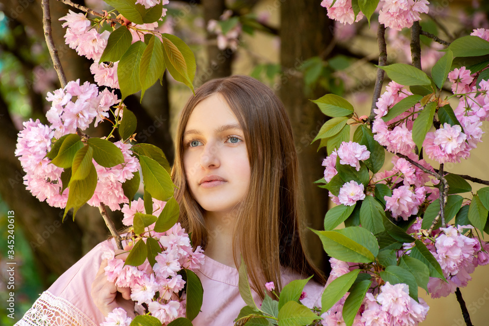 Fototapeta premium Portrait of a beautiful teenage girl in delicate sakura flowers
