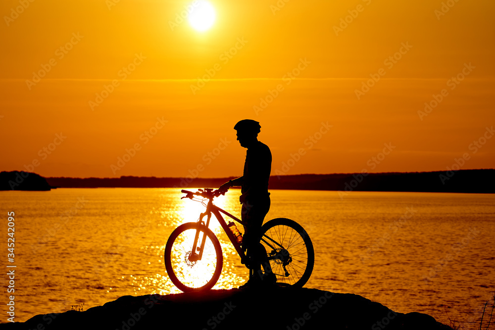 Obraz premium Silhouette of the cyclist riding on a sports bike at sunset. Active lifestyle concept.