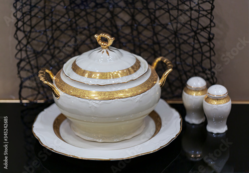 selective focus of salt and pepper shakers with a luxury porcelain tureen with gilding on the table. Close up photo