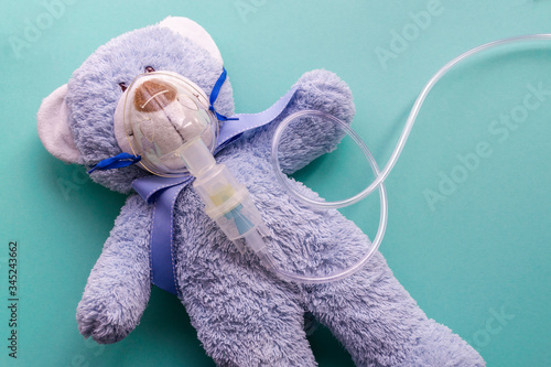 Medicine layout or flat lay. Children's toy masked by inhaler. The blue bear symbolizes the child and childhood.