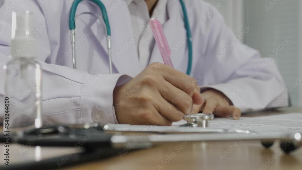 The hand of a female doctor is writing information on the paper, focusing on her right hand. The hand of a female doctor is writing information on the paper, focusing on her right hand.