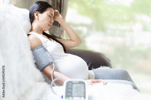 Asian pregnant woman is monitor blood pressure while she has headache to prevent hypertension during pregnancy period, concept of healthcare, sickness and health concern in high risk group pregnancy.