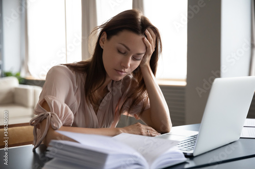 Tableau sur toile Tired sleepy woman sitting at desk with laptop, holding head, resting on hand, s
