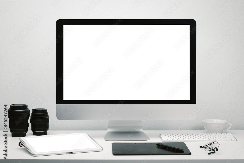 Photographer workspace with blank screen computer display and tablet for mockup on work desk with keyboard, mouse, camera lens, eyeglasses, coffee cup and pen tablet. Photographer workspace with blank screen computer display and tablet for mockup on work desk with keyboard, mouse, camera lens, eyeglasses, coffee cup and pen tablet.