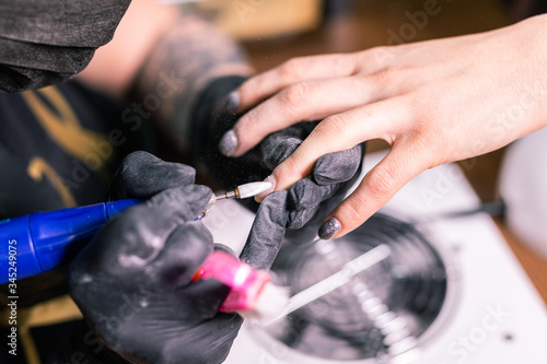 Close-up of manicurist woman removes gel shellac polish from client's nails using manicure machine. Manicure master is working with electric nail drill in beauty salon. Hardware manicure process. © satura_