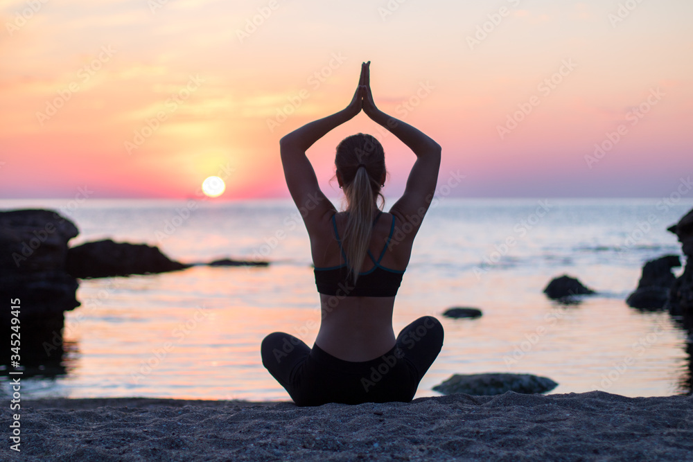 girl has a yoga practice on the beach among big stones. rocks in the sea. sunrise time