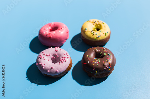 Colourful round donuts at bright blue background. Sweet donuts. Trendy sunlight Summer pattern Minimal summer concept.