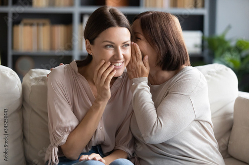 Bild auf Leinwand Middle aged mother whispering in smiling adult daughter ear, gossiping, sharing