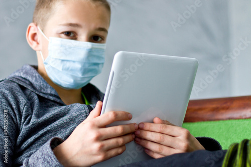 Boy sitting with tablet in mask during quarantine at home