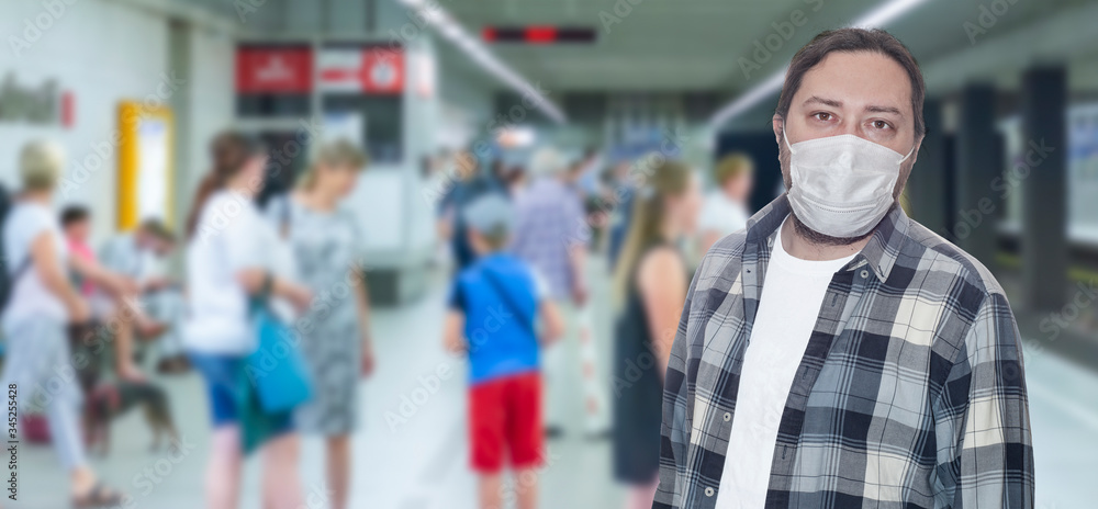 A middle-aged man in a protective mask stands on a subway platform waiting for a train. The concept is virus protection in public transport.