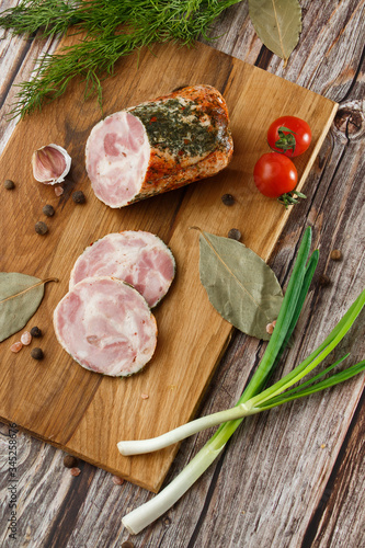 Chicken roll in grid decorated lettuce leaf isolated on wooden background. Fresh meat product whole and partly sliced. Chicken ham, and slices of tasty chicken meat. Natural product from organic farm.