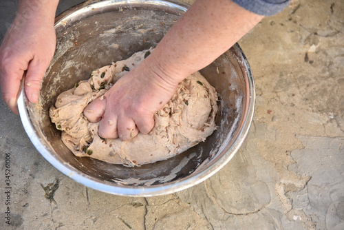 Close up of a baker kneading bread dough in a metal bowl. 
Handmade bread dough in a stainless steel bowl.