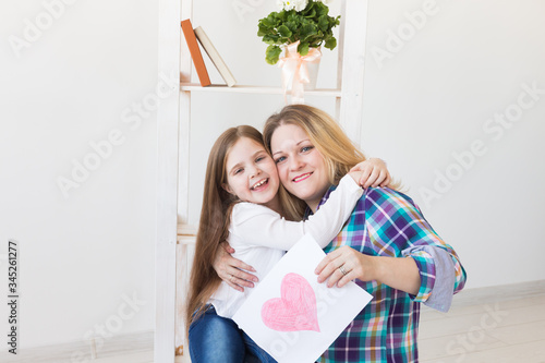 Happy mother's day. Child daughter congratulates mom and gives her postcard. Mum and kid girl smiling and hugging. Family holiday and motherhood.