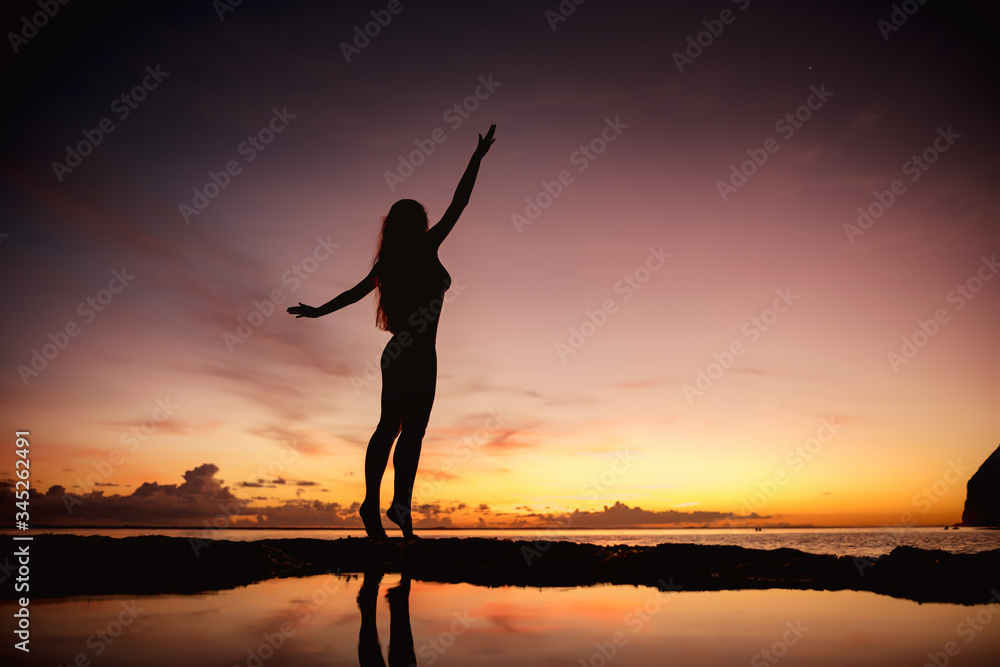 Happy woman in swimsuit with raised arms at sunset beach