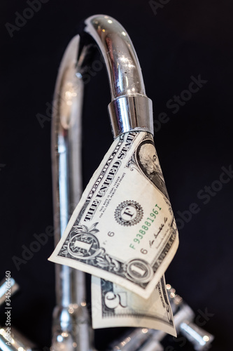 Abstract picture showing how we waste money through leaking taps with dollar bill coming out of the faucet