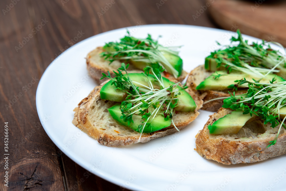 sandwiches with avocado and microgreens on a white plate close-up. healthy breakfast option.