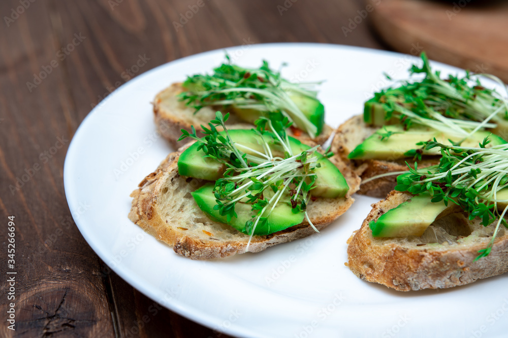 sandwiches with avocado and microgreens on a white plate close-up. healthy breakfast option. sandwiches with avocado and microgreens on a white plate close-up. healthy breakfast option.