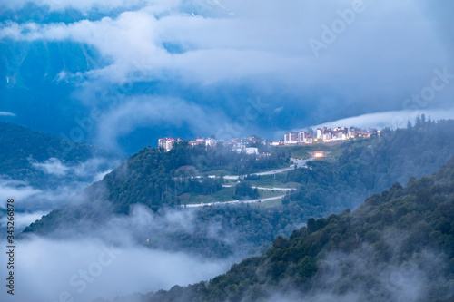 Hotel in the mountains among the green forest. Beautiful clouds and heavy fog at sunset in the mountains. Krasnaya Polyana, Sochi, Russia