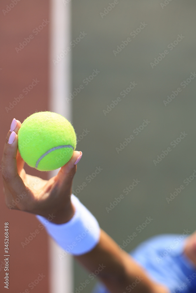 Woman holding a tennis ball with tennis court in the background.