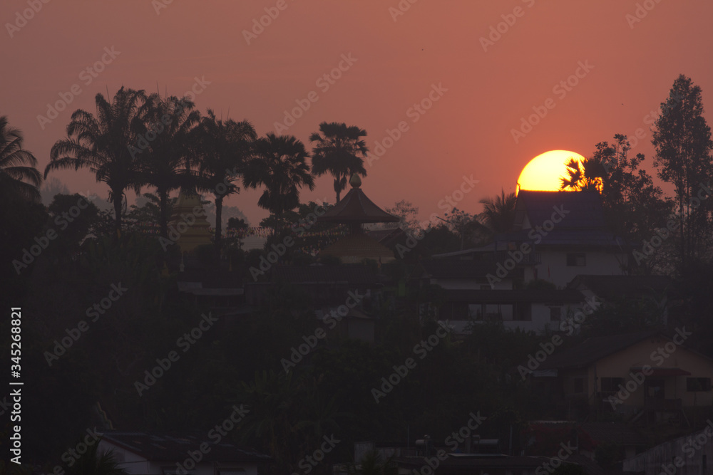 Obraz premium Beautiful Sunrise Behind a Temple and Palms at Laos, seen from Chiang Khong, Thailand, Asia