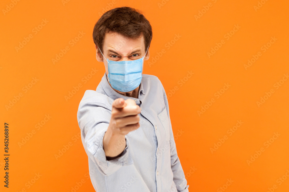 Hey you. Portrait of angry young worker man with surgical medical mask standing pointing and scolding at camera with mad face. indoor studio shot isolated on orange background. Hey you. Portrait of angry young worker man with surgical medical mask standing pointing and scolding at camera with mad face. indoor studio shot isolated on orange background.