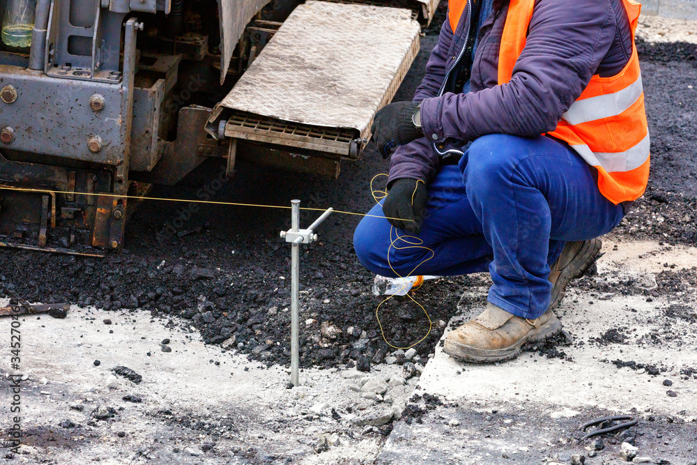 A worker with a stretched thread sets the necessary level for the subsequent asphalting of a new section of the road. A worker with a stretched thread sets the necessary level for the subsequent asphalting of a new section of the road.