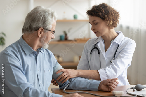 Female professional doctor examining elderly old male patient measuring high low arterial blood pressure using medical tonometer at hospital checkup appointment visit. Seniors hypertension concept.