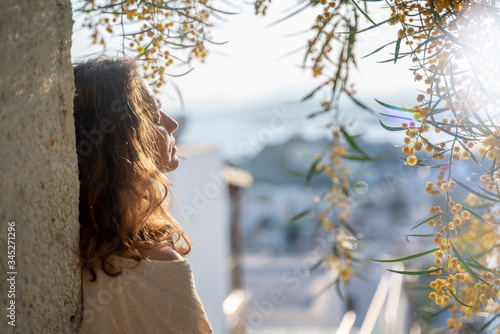 Young beautiful woman girl enjoys morning spring sunshine and blooming mimosa with closed eyes  nature pleasure meditation concept