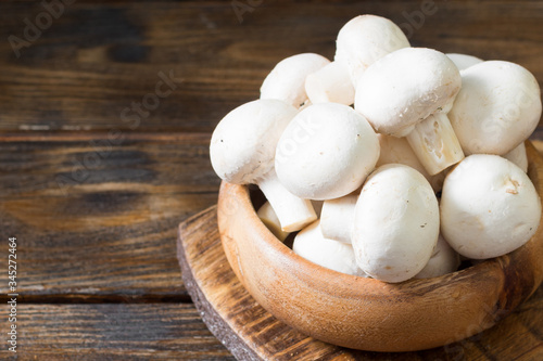Raw mushrooms in a wooden bowl on a brown wooden table. Mushrooms close up with space for text